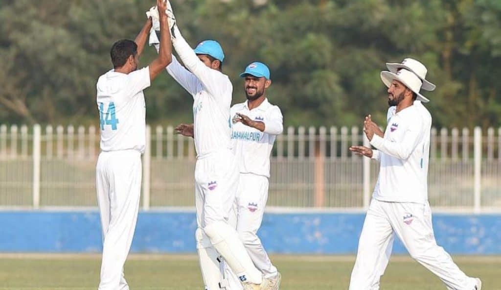 Cricket team celebrating a wicket during Quaid-e-Azam Trophy 2024 match.