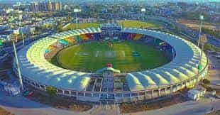 Daylight view of Karachi National Stadium in Pakistan, showing colorful seating, a green cricket field, and modern stands