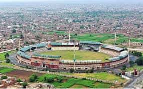 Daylight view of Rawalpindi Cricket Stadium in Pakistan, with green seating, a pristine cricket field, and a modern pavilion