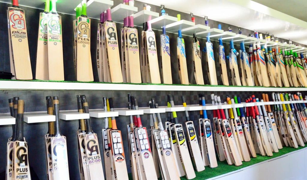 A display of premium cricket bats arranged neatly on shelves in a sports shop, showcasing various brands and models with vibrant designs.